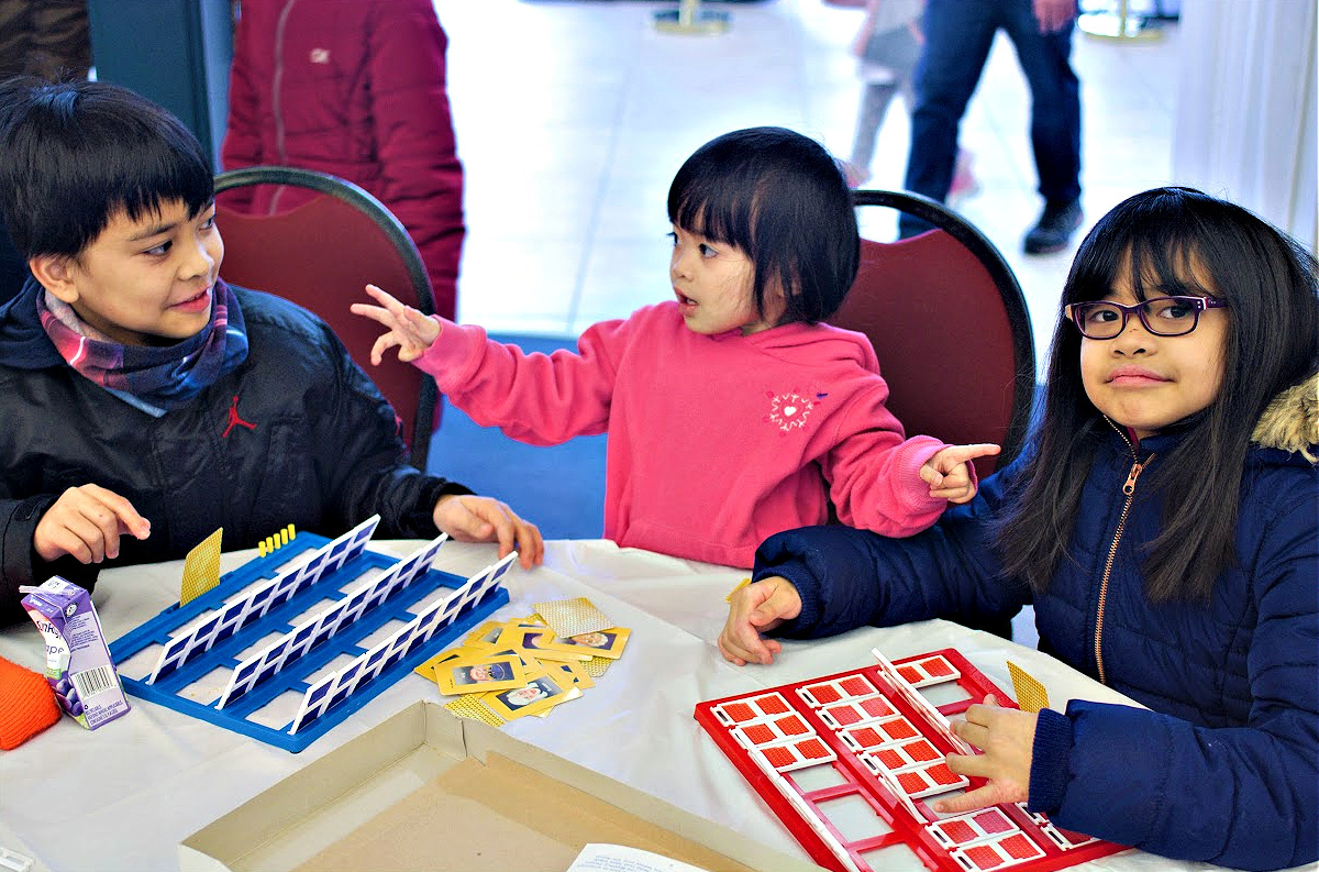 Three siblings, two sisters and a brother sitting at a table playing a boardgame.