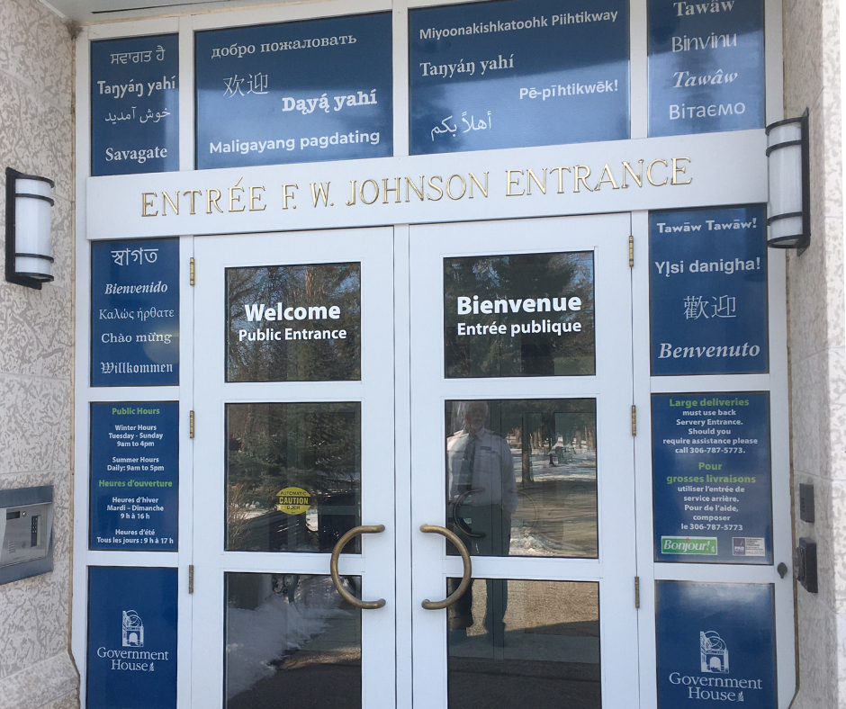 Entrance doors to Government House SK with the word "welcome" in many different languages posted around the doors.