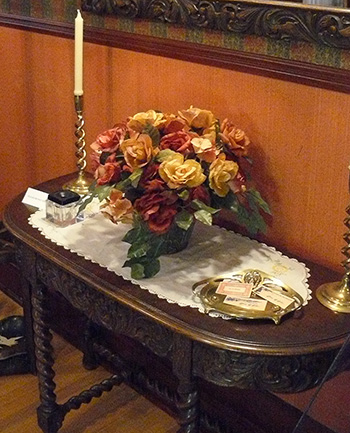 A brass calling card tray on a table which also holds flowers, a ink well and brass candle stick