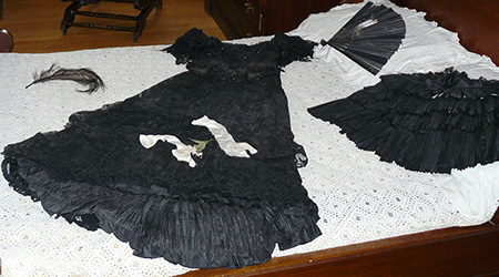 A woman's outfit (black dress, fan, hair piece) laid out on a bed