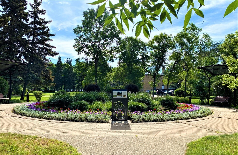 F.W. Johnson Liberation Memorial Garden - June 2022 - which has green-silver plants, red and purple flowers and lots of tall green plants.