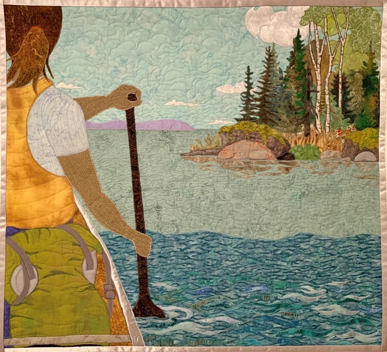 Quilted image of the back of a woman paddling at the front of a canoe with a view of an island on the lake to the right of the canoe..
