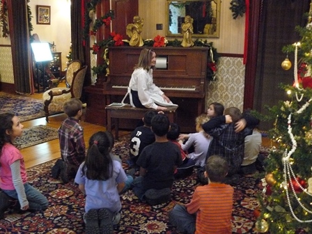 Visitor Experience Host at the player piano with a group of students sitting on the floor.