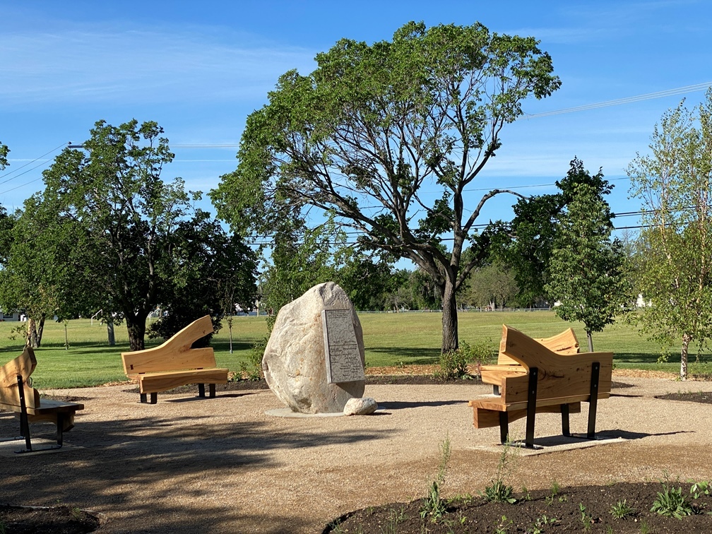 Saskatchewan Residential School Memorial which sits on the grounds of Government House consists of a boulder, with a map showing the locations of Sask residential schools surrounded by a dirt circle which contains four wooden benches which is then surrounded by four gardens with native plants and trees.