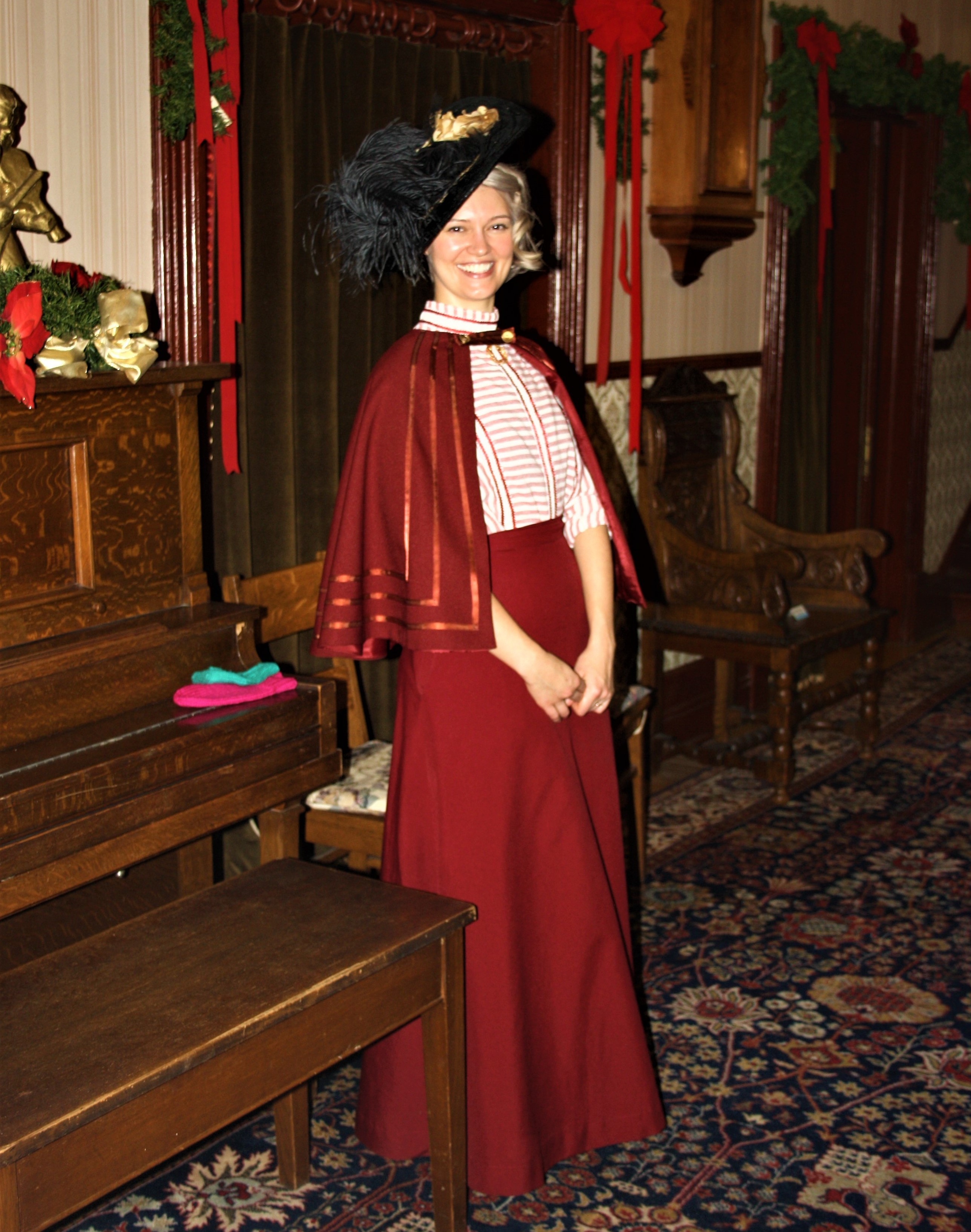 A young woman dressed in Victorian costume standing by a piano in the main hall of the Government House SK
