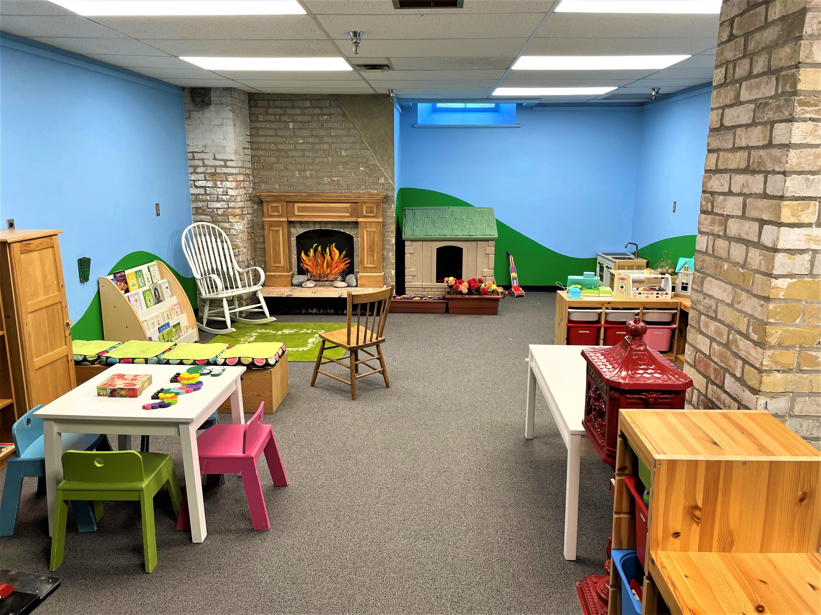 A room set up for young children to play with a rocking chair, a toy house, books, puzzles, etc.